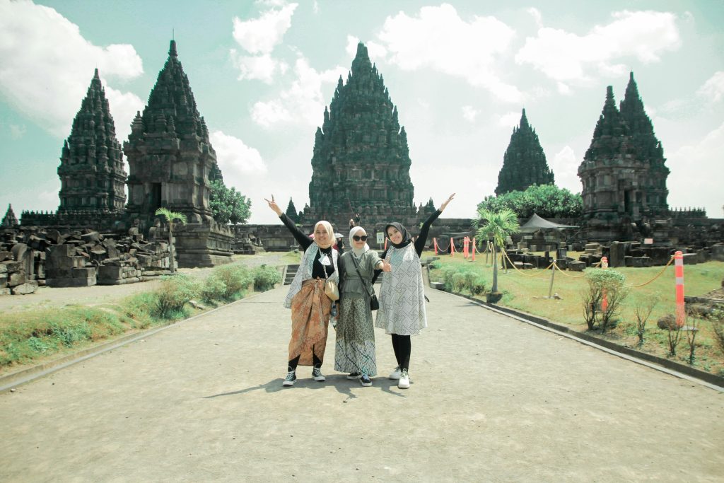 Three women pose happily at the historic Prambanan Temple, a cultural landmark in Jogja, Indonesia.